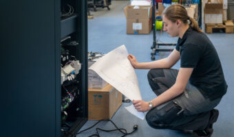 Eine Frau kniet am Boden vor einer Anlage und studiert einen Schaltplan.