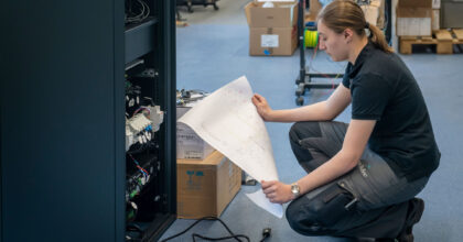 Eine Frau kniet am Boden vor einer Anlage und studiert einen Schaltplan.