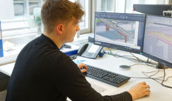 Ein Mann schaut sich an zwei Computerbildschirmen Pläne einer Brücke an.