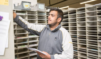 Ein Mann steht vor einer Wand mit vielen Fächern und sortiert Briefe ein.