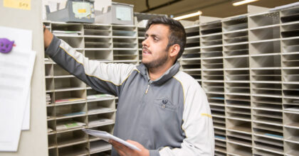 Ein Mann steht vor einer Wand mit vielen Fächern und sortiert Briefe ein.