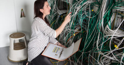 Eine Frau kniet am Boden vor einer Anlage mit sehr vielen Kabeln.