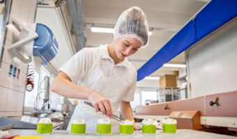 Eine junge Frau dekoriert in einer Backstube mehrere Gebäckstücke.