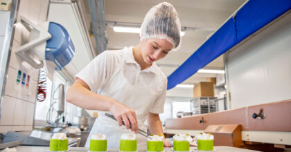 Eine junge Frau dekoriert in einer Backstube mehrere Gebäckstücke.