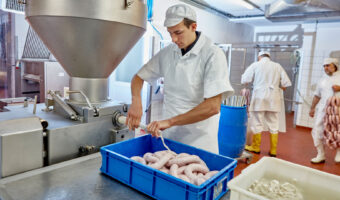 In einer Metzgerei füllt ein Mann Würste in eine Wursthülle.