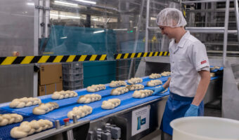 Ein Mann steht an einem Fliessband mit ungebackenen Zöpfen.