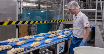 Ein Mann steht an einem Fliessband mit ungebackenen Zöpfen.