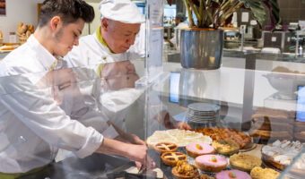Zwei Männer drapieren süsse Köstlichkeiten in einer Vitrine.