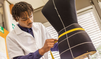 Ein Mann misst mit einem Centimetermass an einer Schneiderpuppe den Taillenumfang.