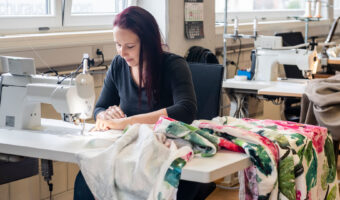 Eine Frau sitzt an einer Nähmaschine und näht an einem bunten Nachtvorhang.