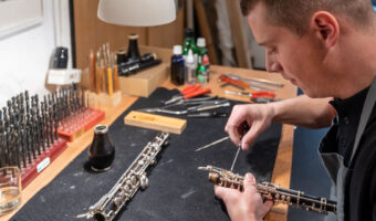 Ein Mann justiert mit einem Werkzeug die Tasten einer Klarinette.