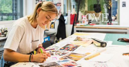 Eine junge Frau sitzt an einem Arbeitstisch und skizziert ein neues Projekt.