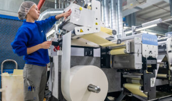 Eine Frau steht an einer Maschine und richtet zu bedruckendes Material für eine Verpackung ein.