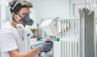 Ein Mann mit Schutzmaske lackiert mit einer Spritzpistole einen Radiator.