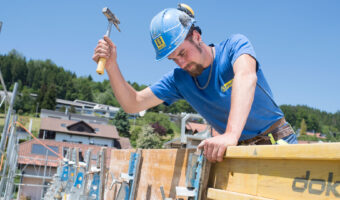 Ein Mann befestigt auf einem Gebäude eine Wandschalung aus Holz.