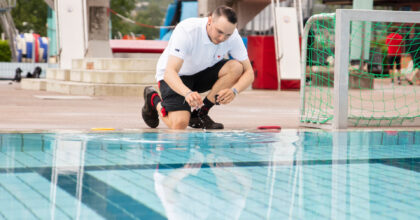 Ein Mann kniet an einem Schwimmbecken in einem Hallenbad und nimmt eine Wasserprobe.
