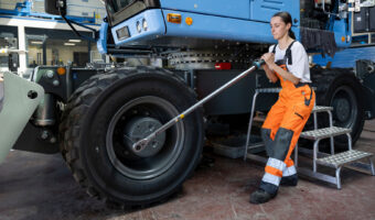 Eine Frau löst an einem Bagger die Radmutter mit einem langen Werkzeug.