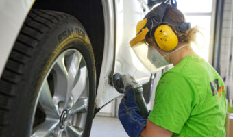 Eine Frau mit Schutzmaske schleift die eingedrückte Tür eines Autos.