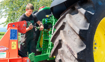Ein junger Mann hantiert an der Anhänger-Kupplung eines Traktors.