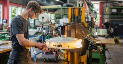 Ein junger Mann mit Schutzbrille hantiert an einem grossen Teil aus Kunststoff.