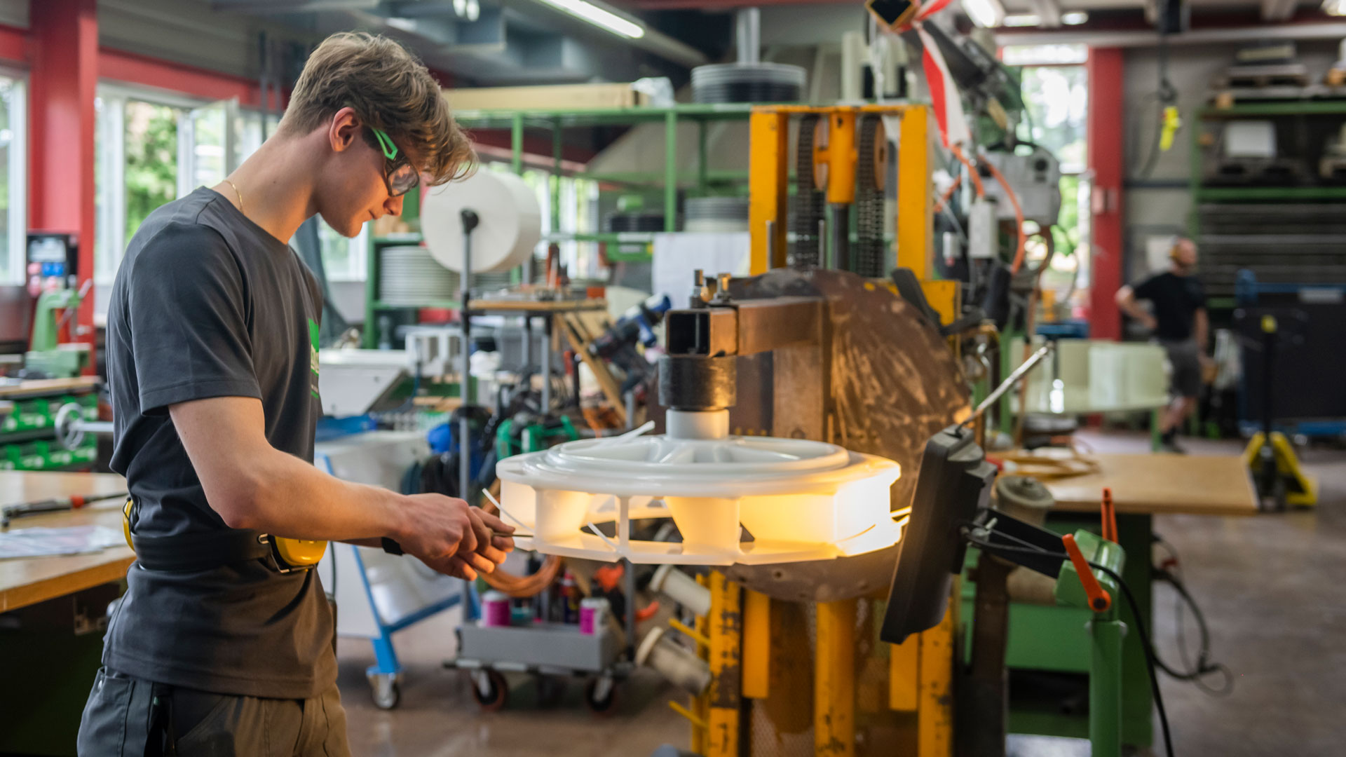 Ein junger Mann mit Schutzbrille hantiert an einem grossen Teil aus Kunststoff.