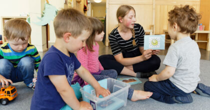 Eine Frau sitzt mit vier kleinen Kindern am Boden und erzählt eine Geschichte.